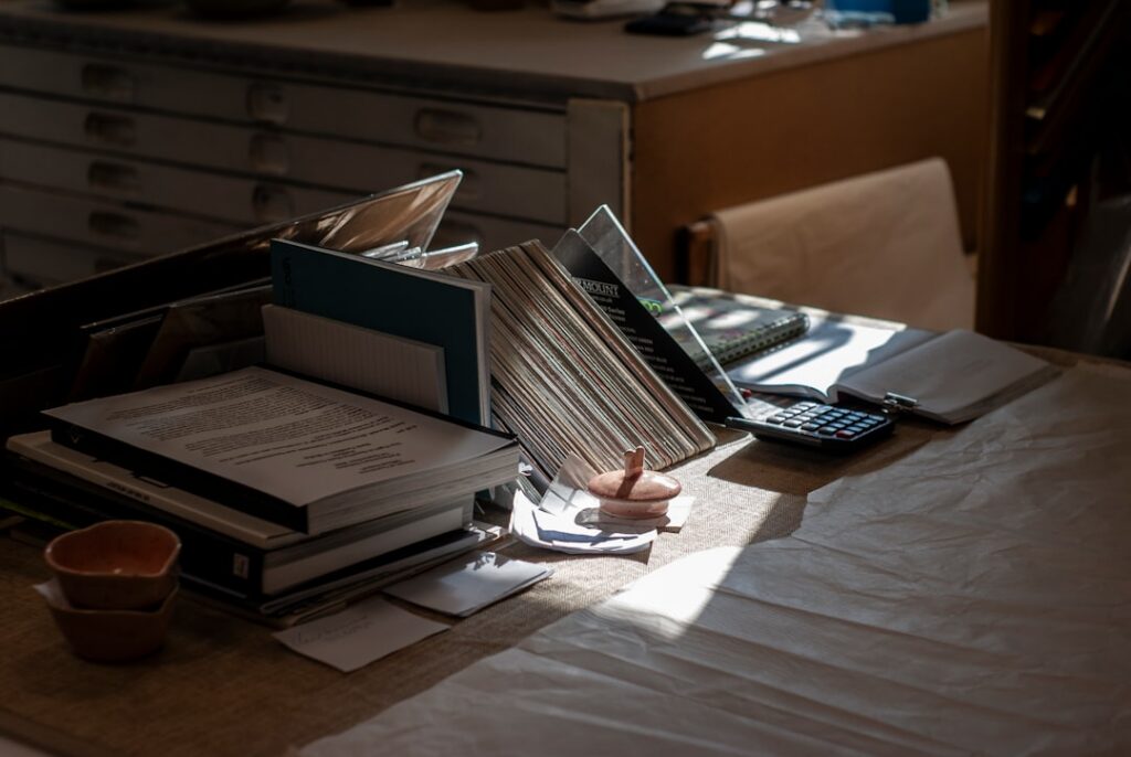 Homeowner sits at a sunlit dining table with a calculator, pen, and a stack of papers, looking concerned as they calculate...