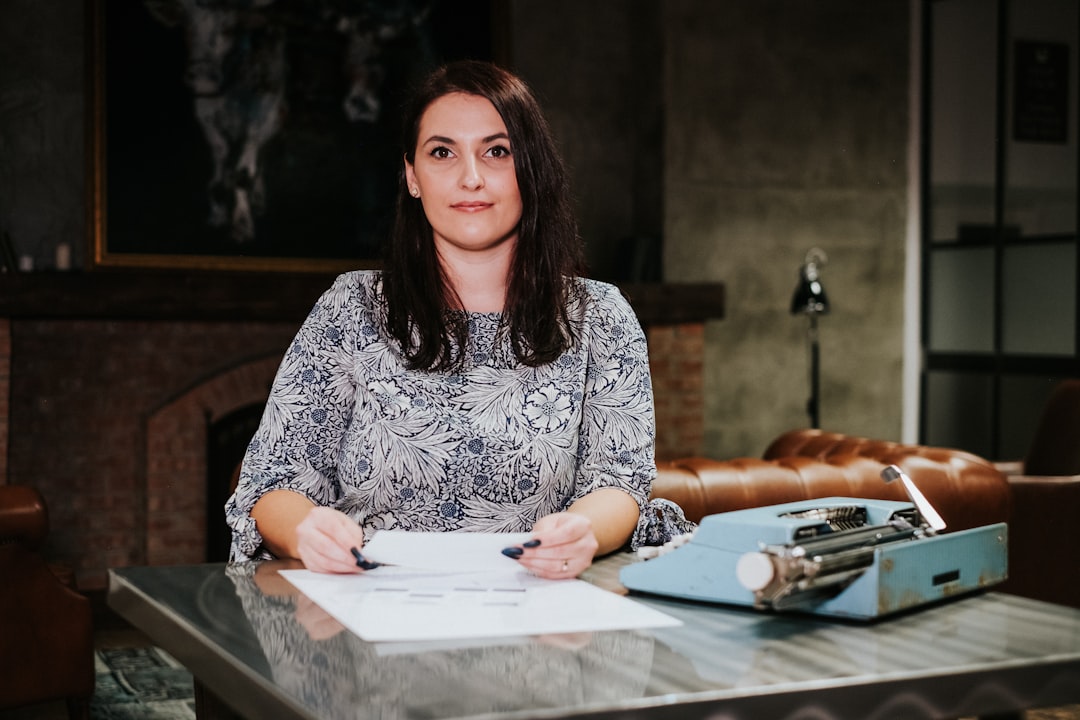 A person sits at a bright, modern desk with a laptop and calculator, carefully reviewing documents to strategically price their home for the market.