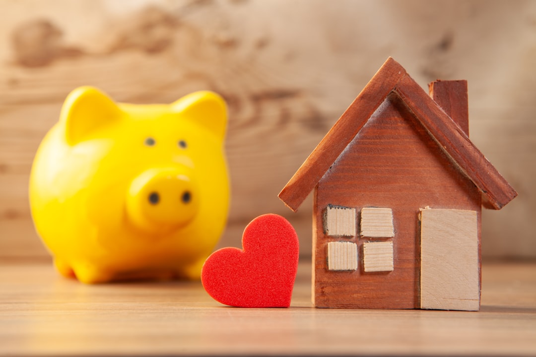 A close-up of a person's hand placing a coin into a house-shaped piggy bank against a clean, minimal background, symbolizing saving equity on a home sale.