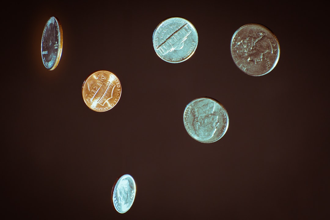 Person's hand lets shiny coins slip through their fingers against a bright, clean background, symbolizing the financial lo...