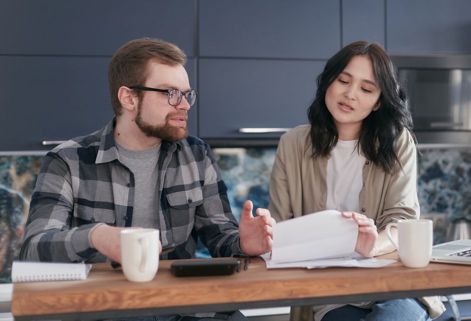 A happy couple sits at a dining room table in a bright, modern home, reviewing paperwork and smiling, representing savvy homeowners making a smart financial decision.