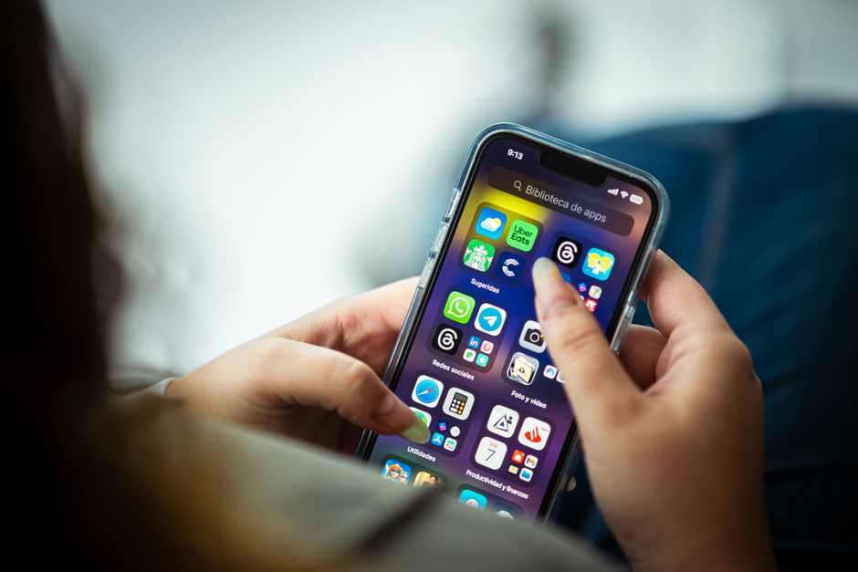 Person stands outside a modern suburban home, viewing a real estate application on their smartphone, illustrating the conc...