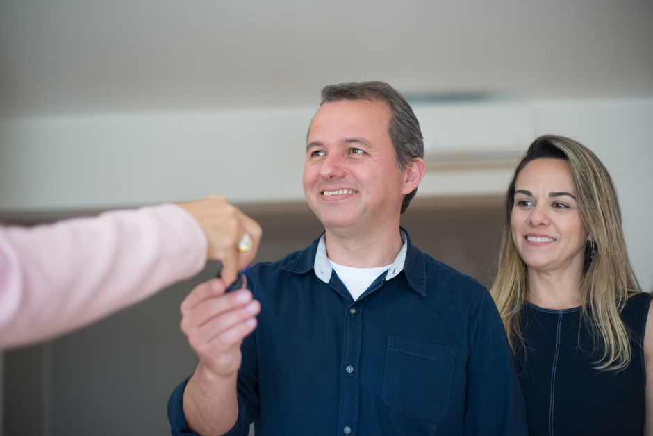A person's hand holding a set of house keys inside a bright, modern kitchen, symbolizing a successful and profitable home sale.