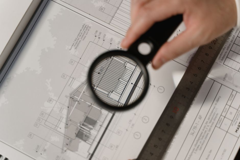 A professional's hands holding a magnifying glass over detailed architectural blueprints on a clean desk, illustrating a commitment to transparency and detail.
