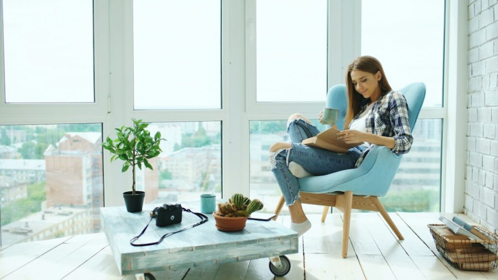 Person sits in a bright, modern living room, holding a tablet that displays beautiful photos of homes for sale on a real e...