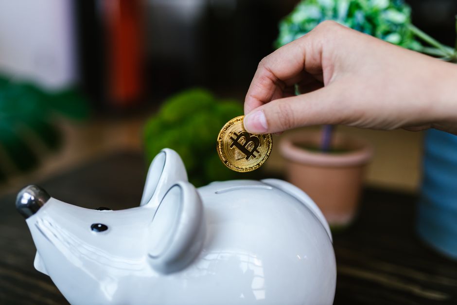 A person's hand placing a coin into a house-shaped piggy bank, illustrating the concept of saving money and protecting home equity.
