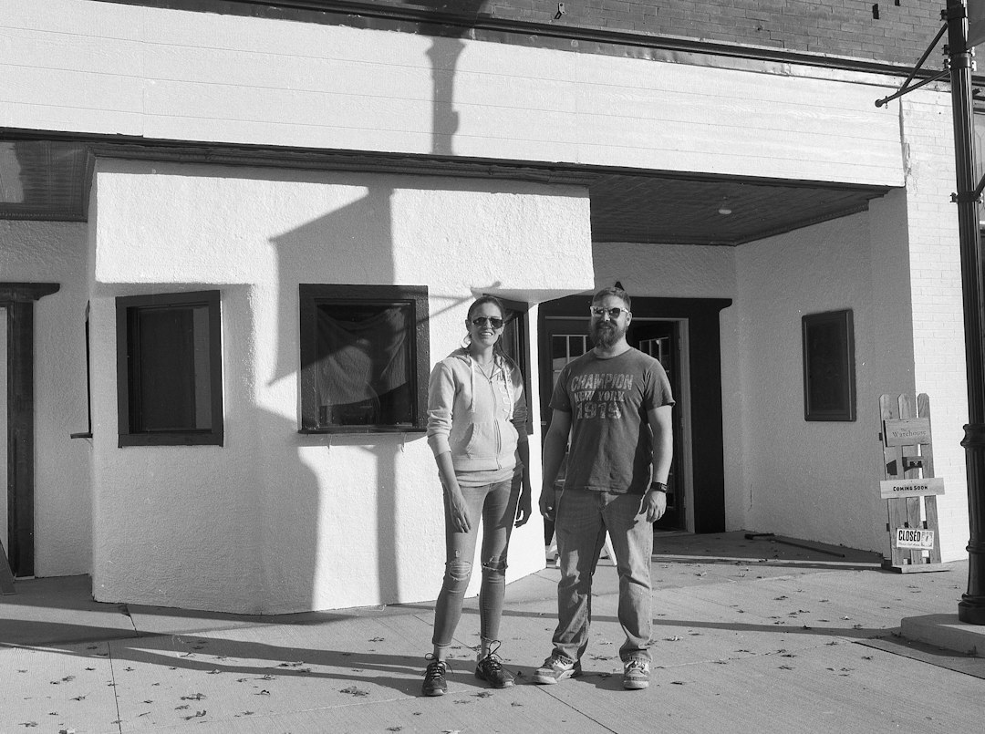 A smiling couple stands proudly in front of their house next to a real estate 'Sold' sign, symbolizing a successful and profitable home sale.