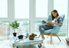 Person sits in a bright, modern living room, holding a tablet that displays beautiful photos of homes for sale on a real e...