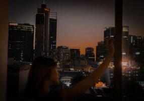 Person stands inside a modern home looking out a large, clean window at the city below, symbolizing gaining clarity on hom...