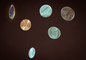 Person's hand lets shiny coins slip through their fingers against a bright, clean background, symbolizing the financial lo...